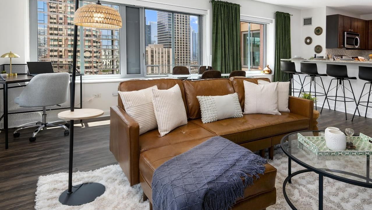 An open-concept living room at Chestnut Towers, showcasing a brown leather sofa, modern decor, and a dedicated workspace