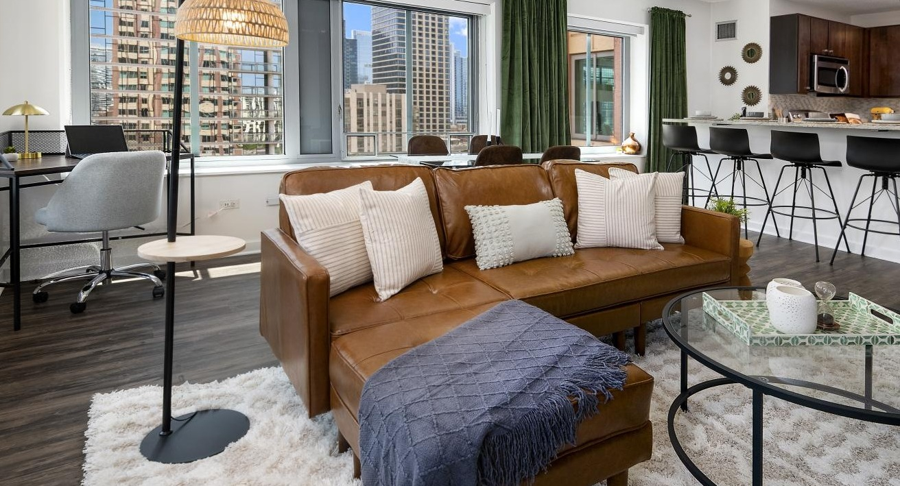 An open-concept living room at Chestnut Towers, showcasing a brown leather sofa, modern decor, and a dedicated workspace