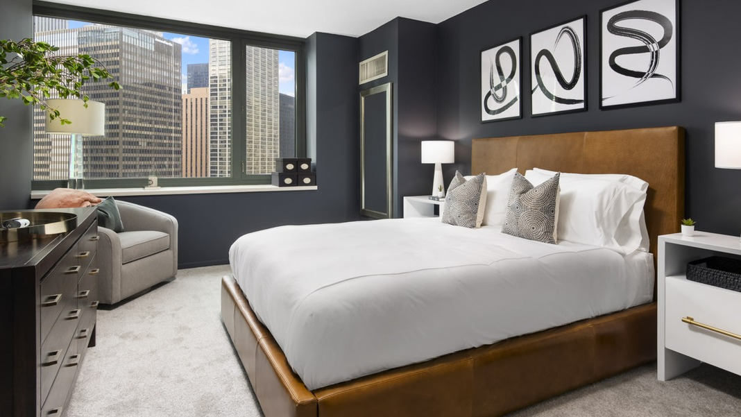 Stylish bedroom at Cityfront Place featuring a leather-frame bed, dark accent wall, and large windows with city views