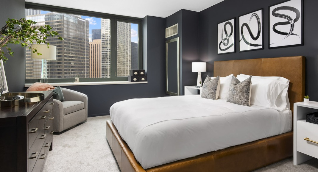 Stylish bedroom at Cityfront Place featuring a leather-frame bed, dark accent wall, and large windows with city views