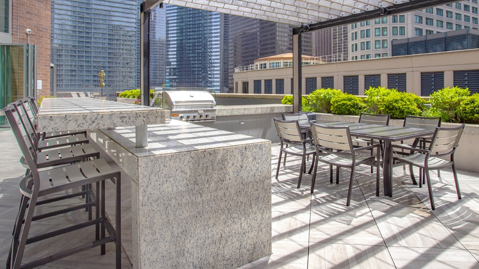 Outdoor grilling and dining area at Cityfront Place with a bar, picnic tables, and shaded seating