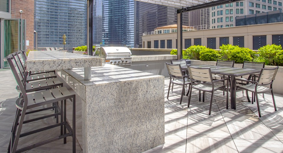 Outdoor grilling and dining area at Cityfront Place with a bar, picnic tables, and shaded seating