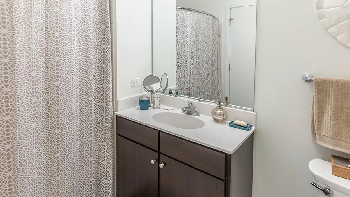 A well-appointed bathroom at Coast at Lakeshore East with a dark wood vanity, framed mirror, and decorative shower curtain