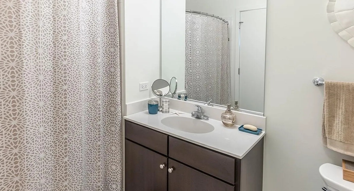 A well-appointed bathroom at Coast at Lakeshore East with a dark wood vanity, framed mirror, and decorative shower curtain