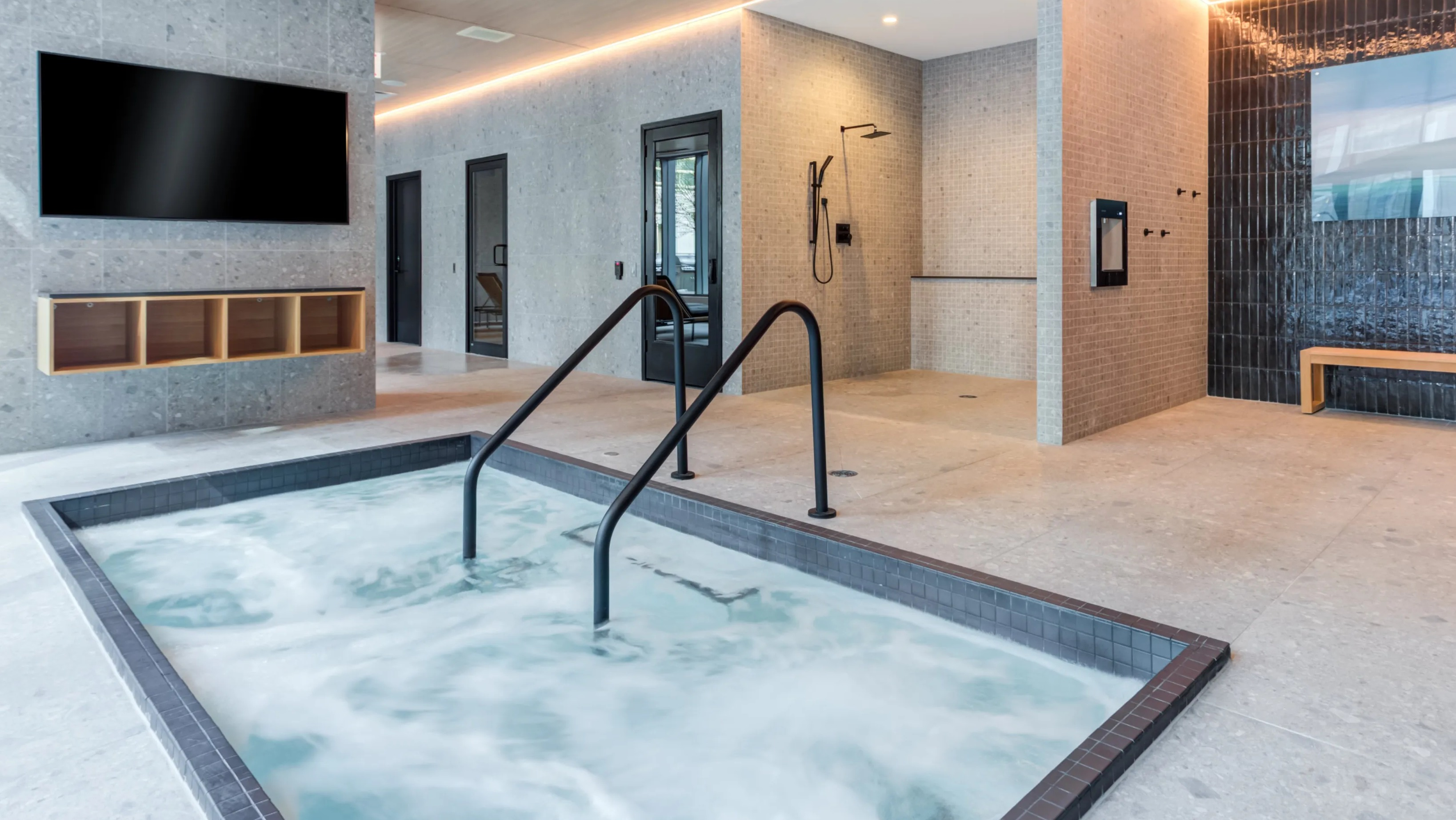 A modern indoor spa area at Coast at Lakeshore East featuring a bubbling hot tub and spacious showers