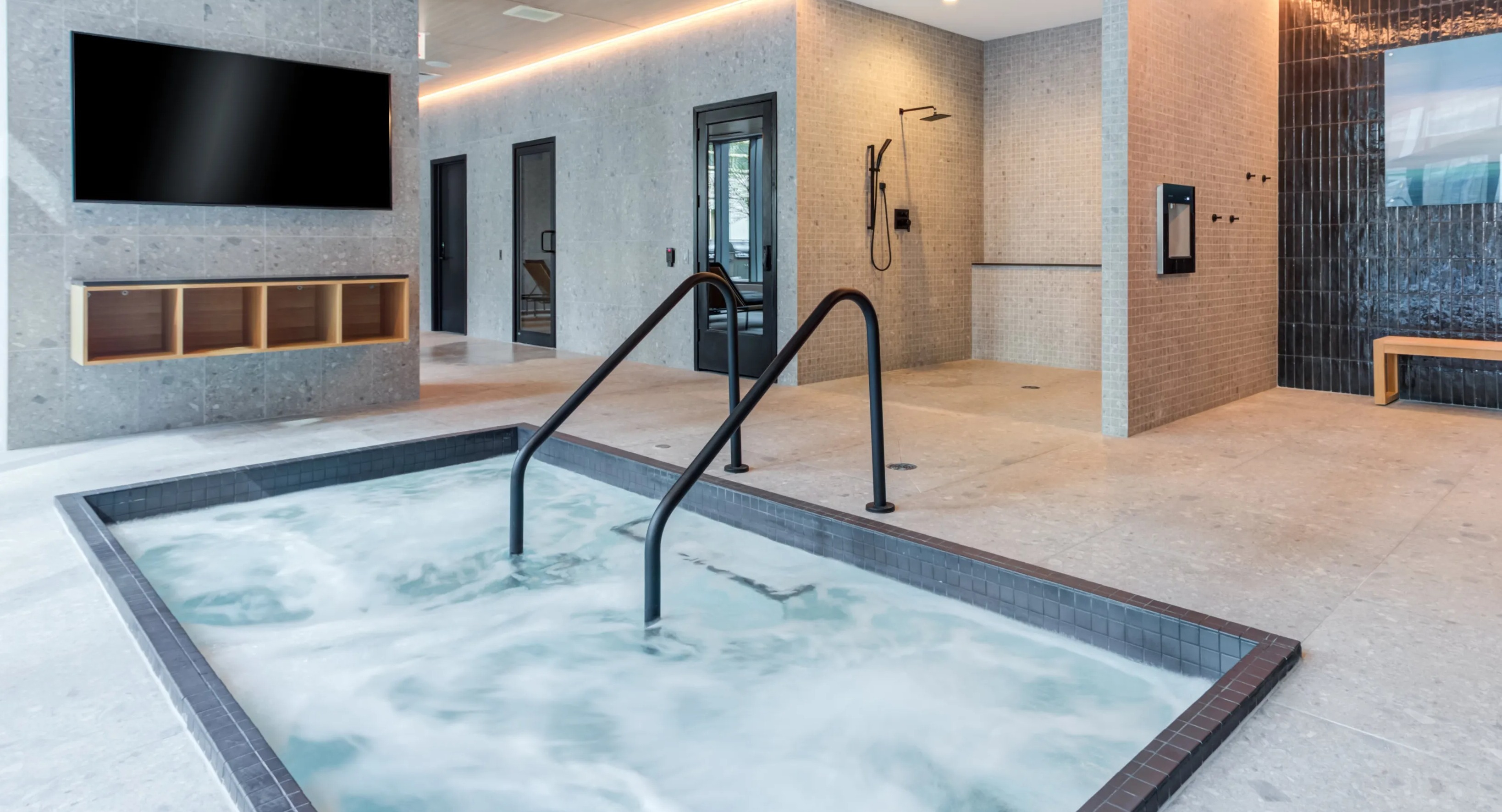 A modern indoor spa area at Coast at Lakeshore East featuring a bubbling hot tub and spacious showers