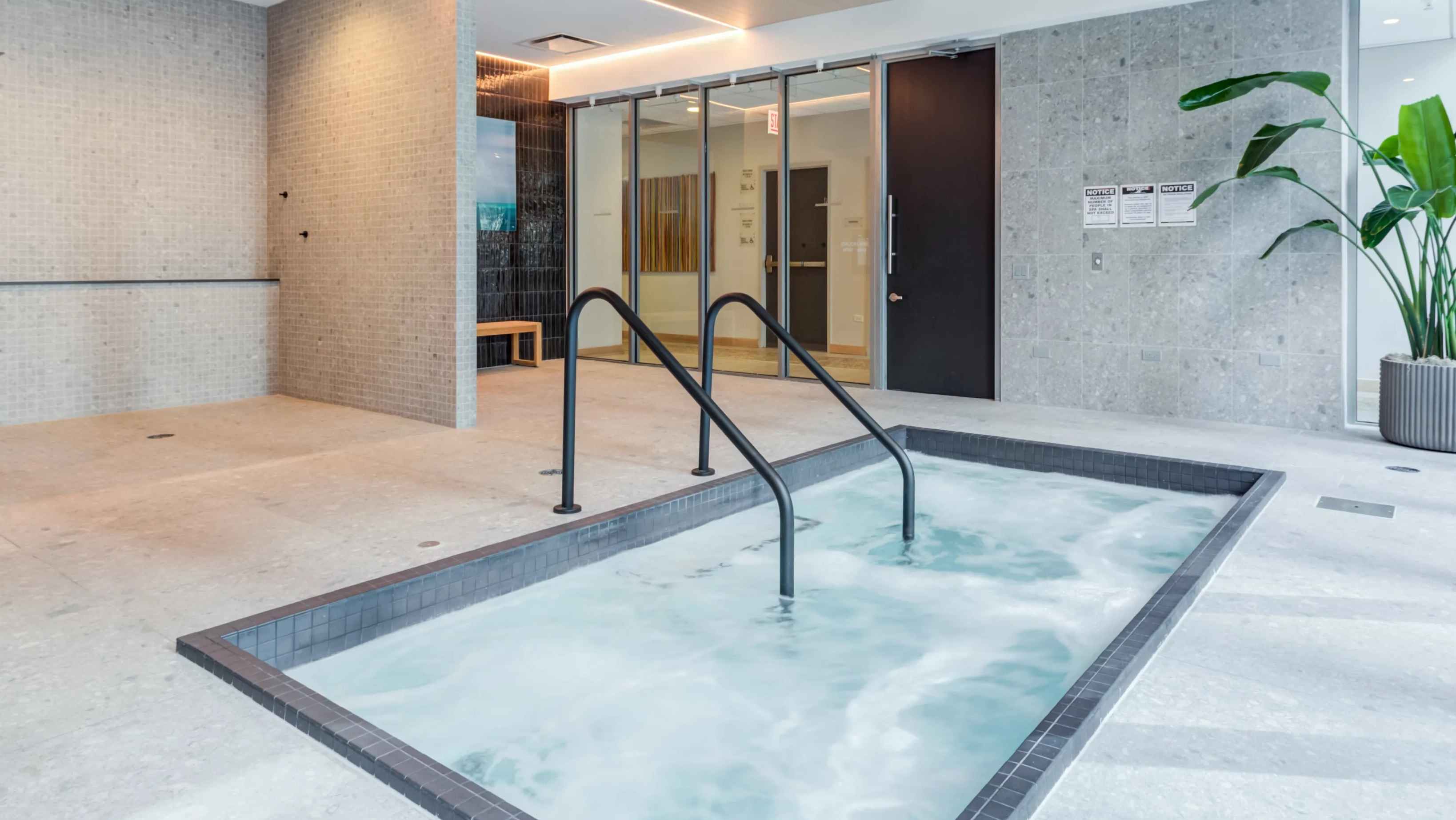 A serene indoor spa area at Coast at Lakeshore East with a hot tub, showers, and a large potted plant