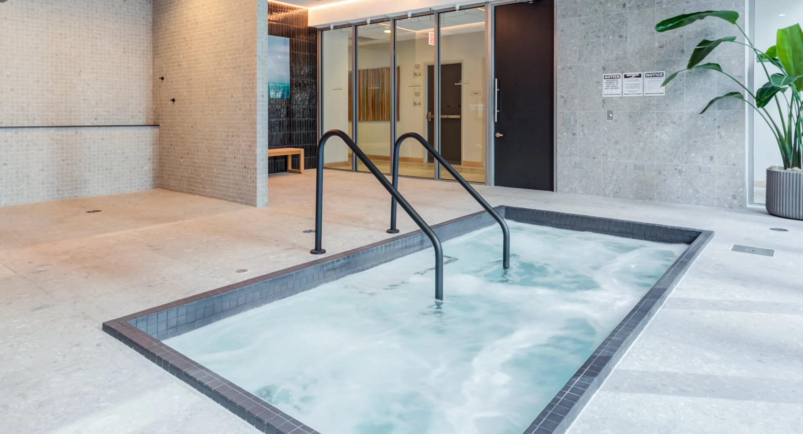 A serene indoor spa area at Coast at Lakeshore East with a hot tub, showers, and a large potted plant
