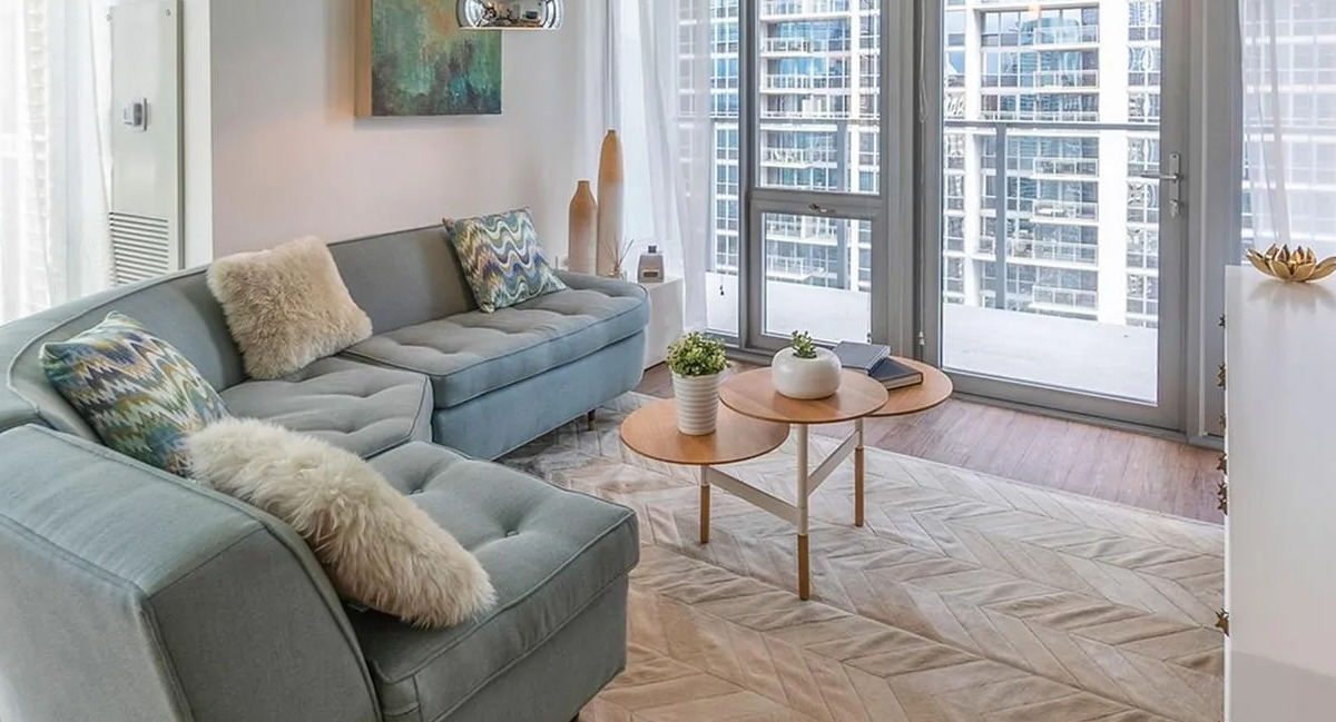 A cozy living room at Coast at Lakeshore East with a curved sofa, patterned rug, and large windows offering city views