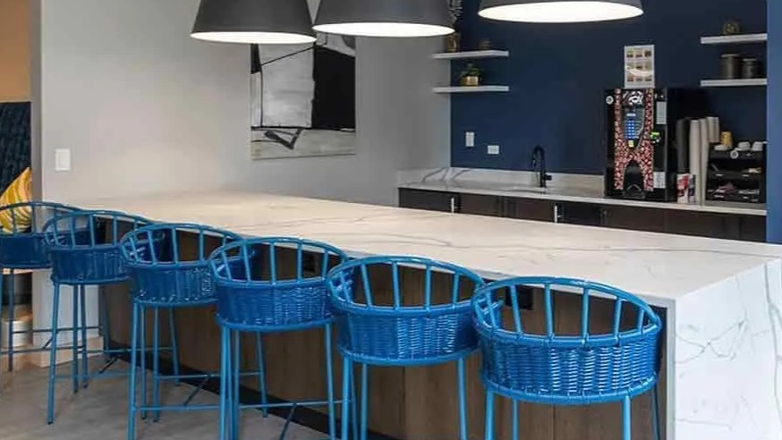 A vibrant communal lounge at Coast at Lakeshore East with a long white counter, blue bar stools, and modern pendant lights
