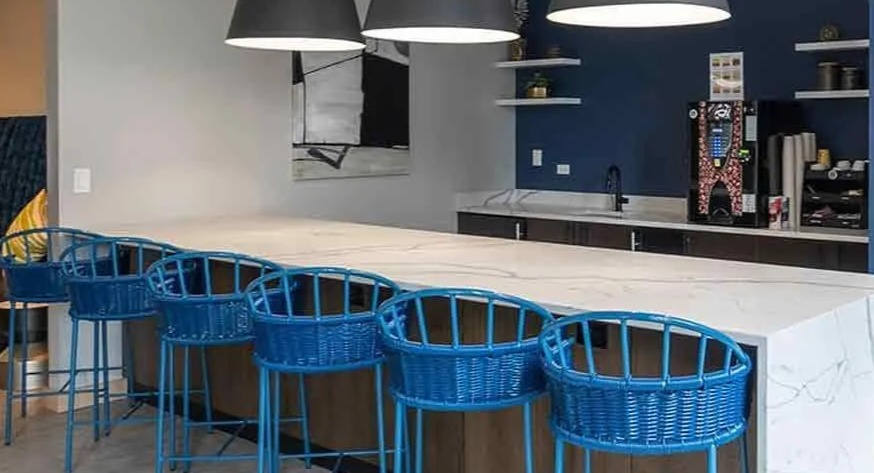 A vibrant communal lounge at Coast at Lakeshore East with a long white counter, blue bar stools, and modern pendant lights