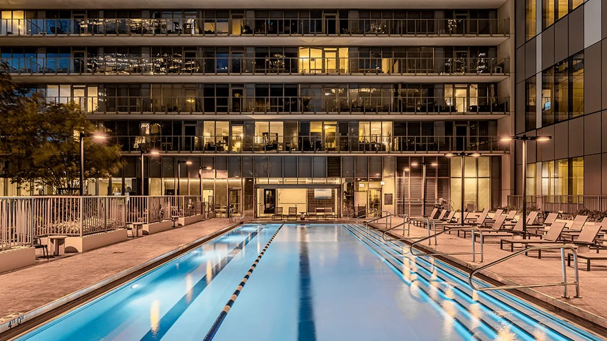 A long, illuminated outdoor swimming pool at Coast at Lakeshore East at night, surrounded by lounge chairs and buildings