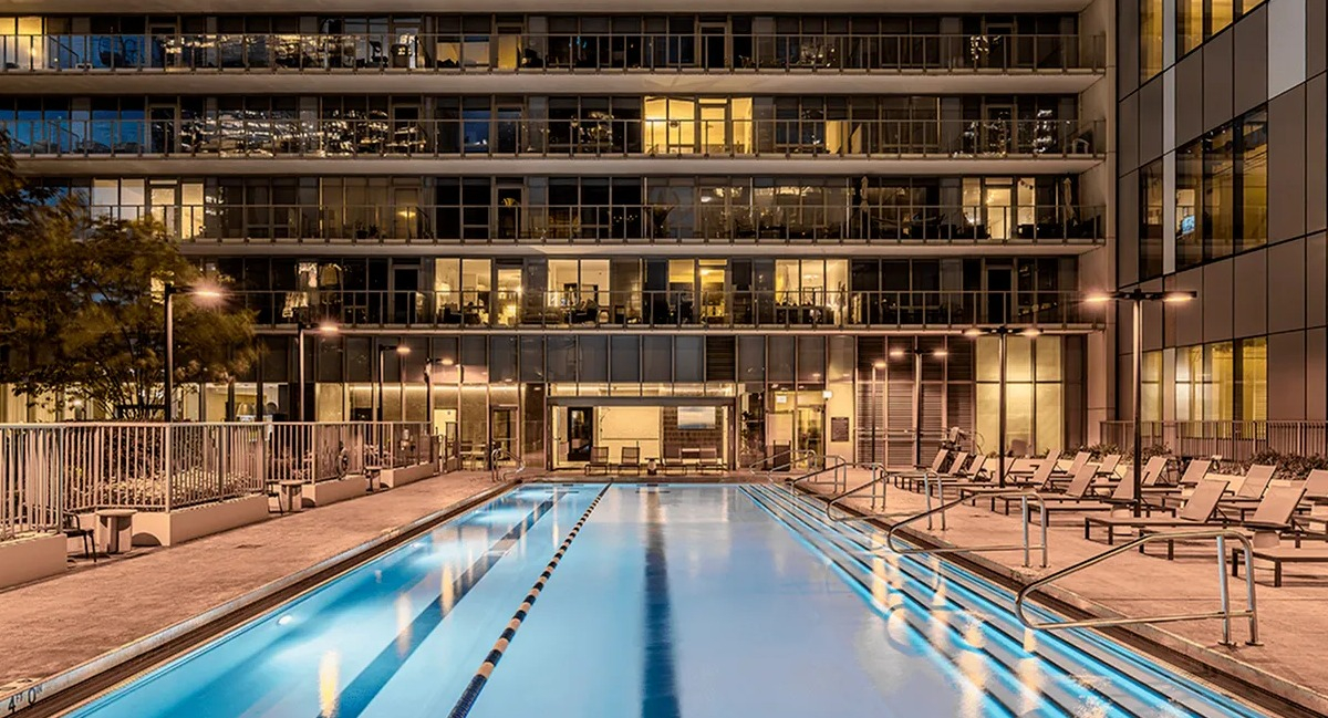 A long, illuminated outdoor swimming pool at Coast at Lakeshore East at night, surrounded by lounge chairs and buildings