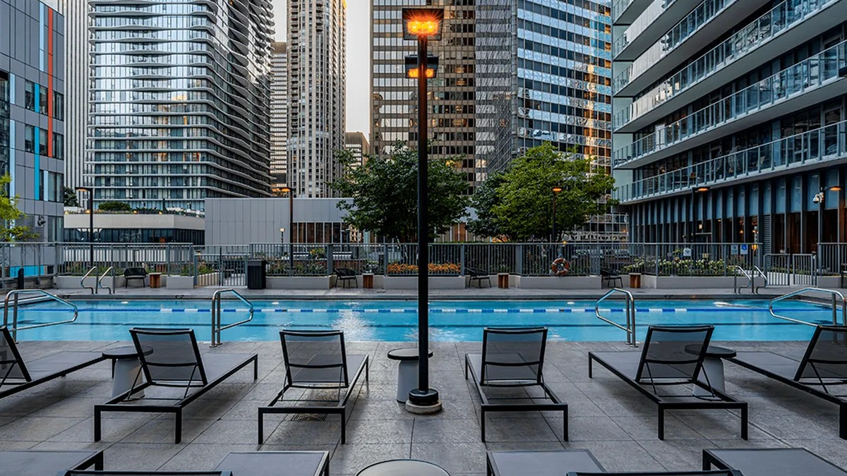 The poolside lounging area at Coast at Lakeshore East with modern chairs, bright lights, and towering city buildings