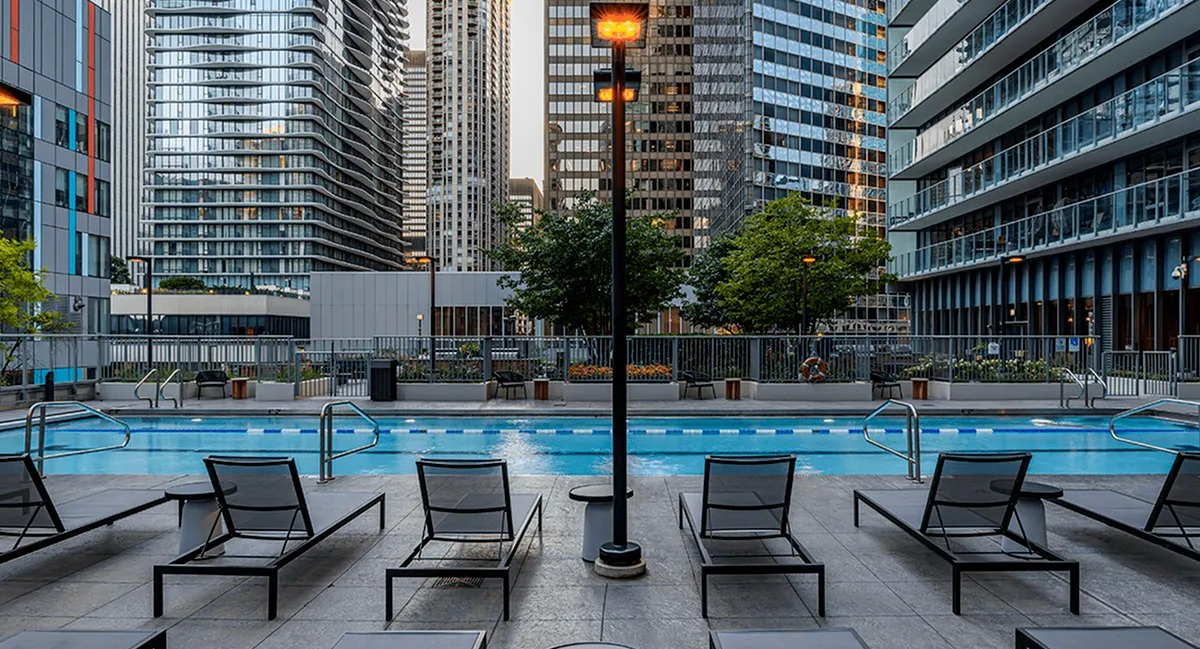 The poolside lounging area at Coast at Lakeshore East with modern chairs, bright lights, and towering city buildings