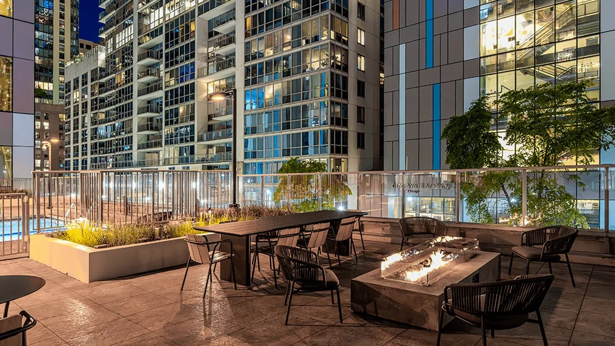 An inviting rooftop deck at Coast at Lakeshore East at night, with a fire pit, seating, and city lights