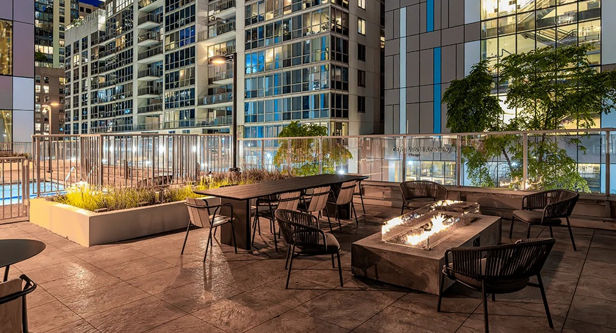 An inviting rooftop deck at Coast at Lakeshore East at night, with a fire pit, seating, and city lights