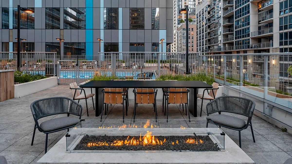 A sunny rooftop deck at Coast at Lakeshore East with a fire pit, barbecue grills, and comfortable outdoor seating