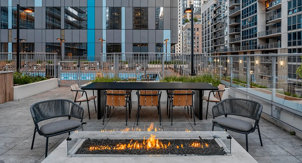 A sunny rooftop deck at Coast at Lakeshore East with a fire pit, barbecue grills, and comfortable outdoor seating