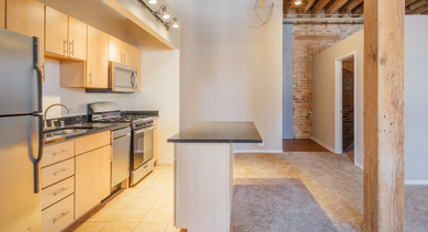 Compact and cozy kitchenette with light wood cabinets, an island, and tiled flooring at Cobbler Square Lofts in Chicago