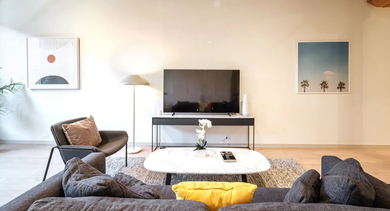 A modern living room with a large TV, comfortable seating, and striking exposed wooden beams at Cobbler Square Lofts in Chicago