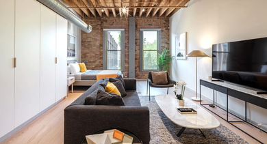 A spacious studio apartment with a comfortable living area, bedroom, and exposed brick walls at Cobbler Square Lofts in Chicago