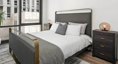 A cozy bedroom with a comfortable bed, stylish nightstands, and a large window offering a city view at Coeval Apartments in Chicago