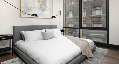 A cozy bedroom featuring a comfortable bed, sleek nightstands, and large windows with city views at Coeval Apartments in Chicago
