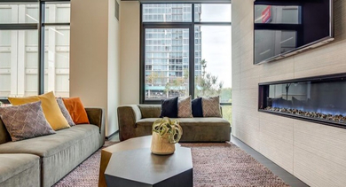Modern living area with plush sofas, a sleek wall-mounted fireplace, and large windows offering city views at Coeval Apartments in Chicago