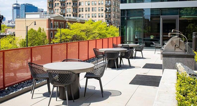 Rooftop patio with several dining tables and chairs, offering city skyline views at Coeval Apartments in Chicago
