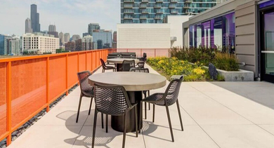 Expansive rooftop patio with dining tables and chairs, overlooking the Chicago city skyline at Coeval Apartments