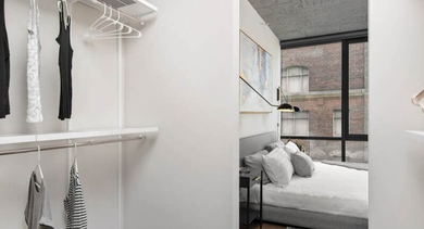 A spacious walk-in closet with shelving and hanging space, offering direct access to a cozy bedroom at Coeval Apartments in Chicago