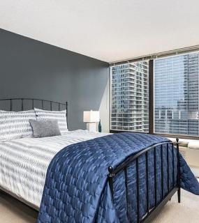 Modern bedroom with a comfortable bed, dark accent wall, and large windows offering stunning city views at Columbus Plaza