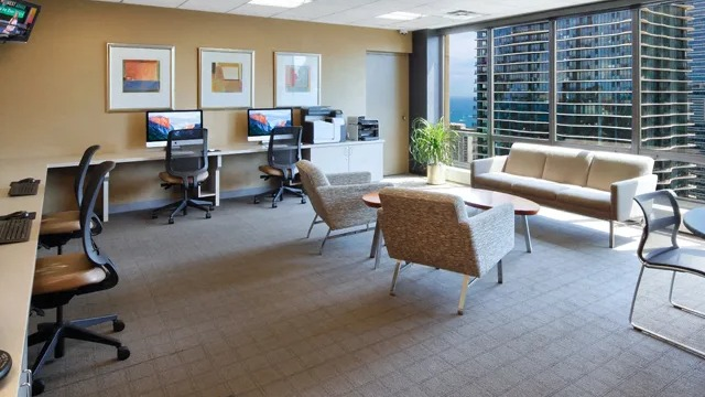 A spacious business center with workstations, comfortable seating, and city views from large windows