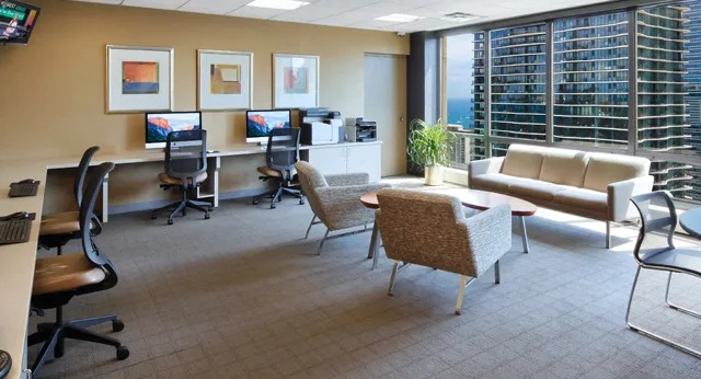 A spacious business center with workstations, comfortable seating, and city views from large windows