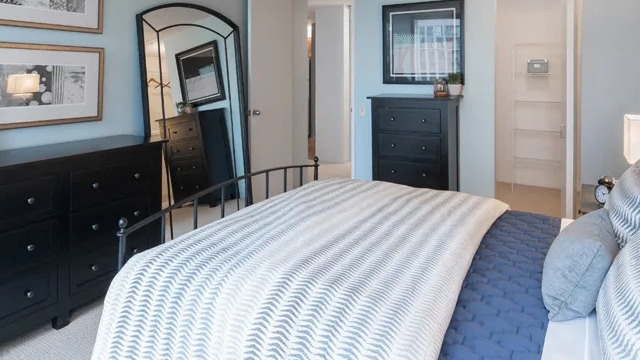 A serene bedroom featuring a large bed with blue and white bedding, dark wood dressers, and a full-length mirror
