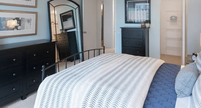 A serene bedroom featuring a large bed with blue and white bedding, dark wood dressers, and a full-length mirror