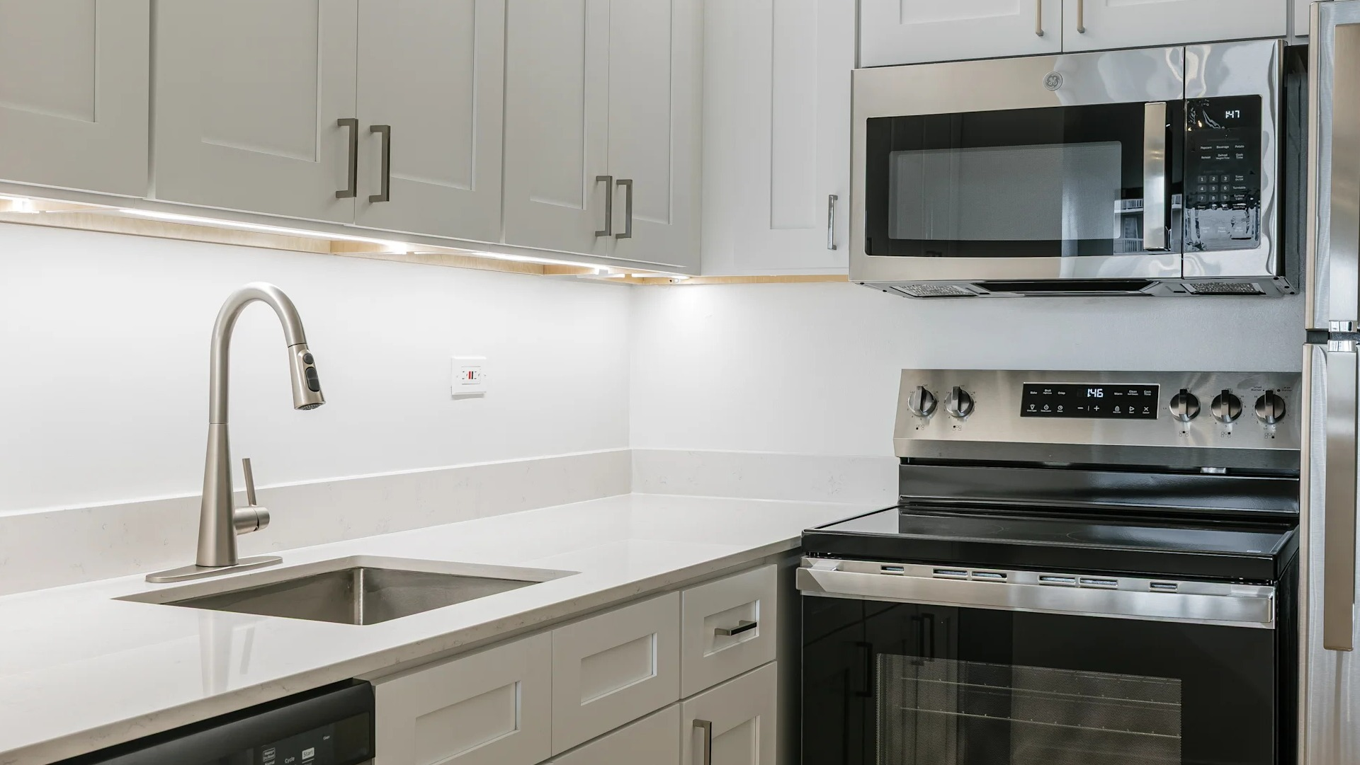A bright, modern kitchen featuring white shaker cabinets, stainless steel appliances, and clean countertops