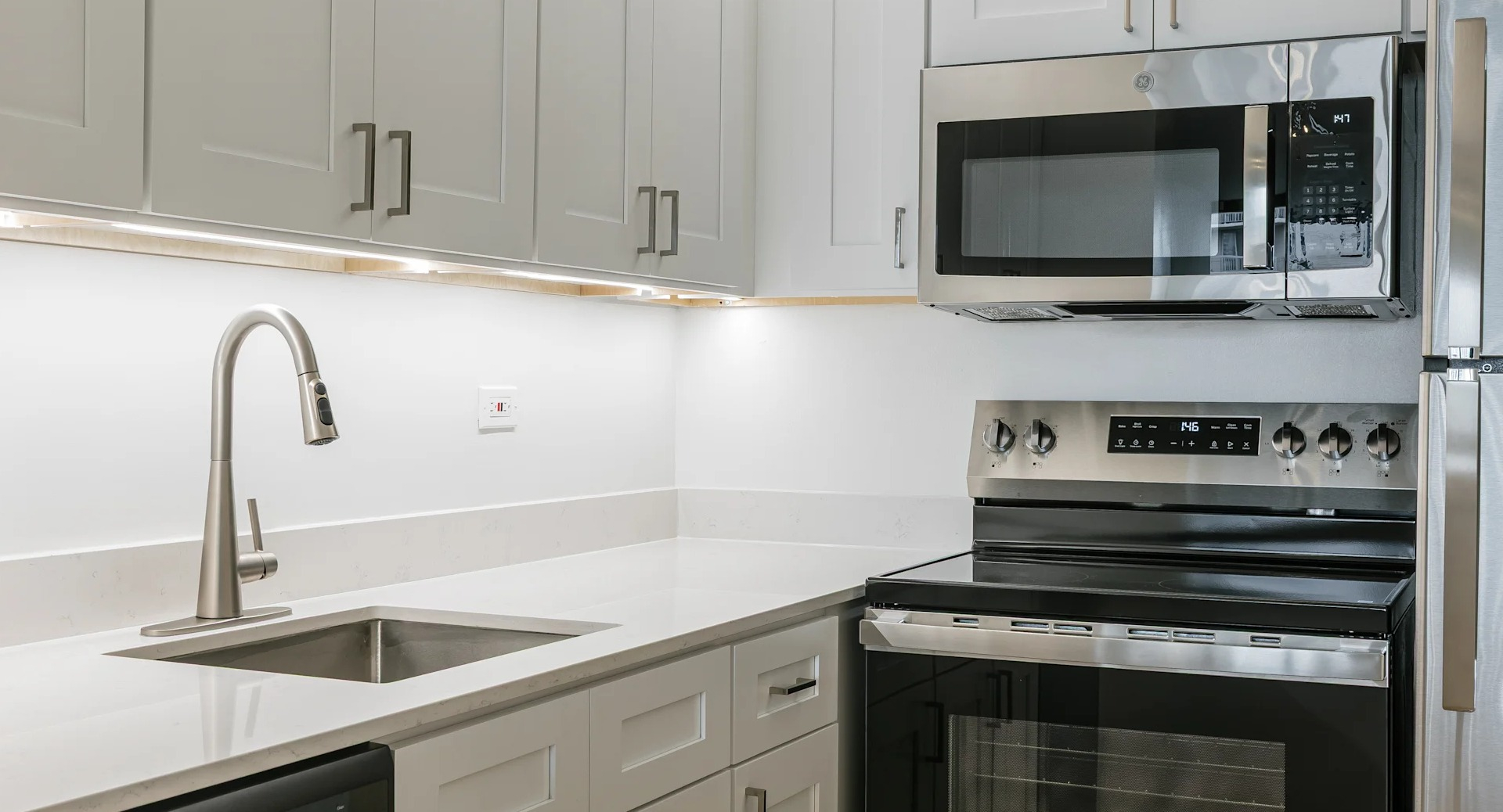 A bright, modern kitchen featuring white shaker cabinets, stainless steel appliances, and clean countertops