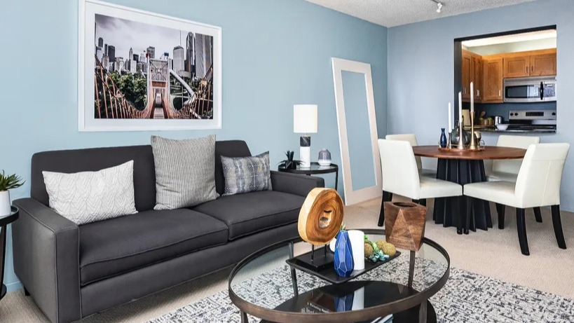A cozy living area with a dark sofa, coffee table, and a dining nook, showcasing modern urban apartment living