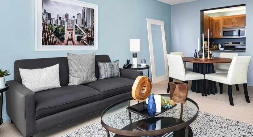 A cozy living area with a dark sofa, coffee table, and a dining nook, showcasing modern urban apartment living