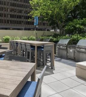 Outdoor BBQ area with modern grills, dining tables, and a lush garden backdrop at Columbus Plaza