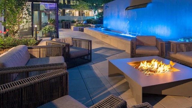 An inviting outdoor lounge area with comfortable seating, a modern fire pit, and a blue lit water feature