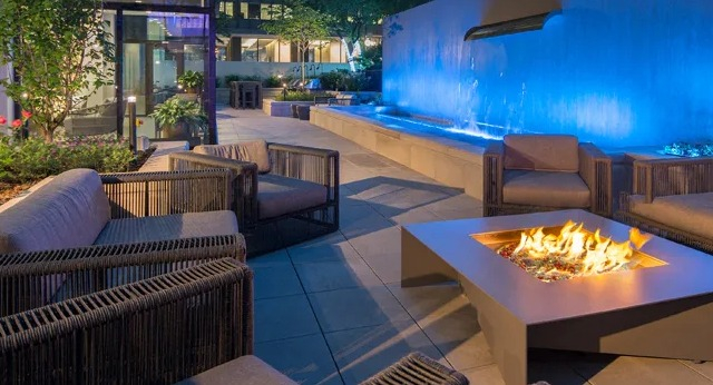 An inviting outdoor lounge area with comfortable seating, a modern fire pit, and a blue lit water feature