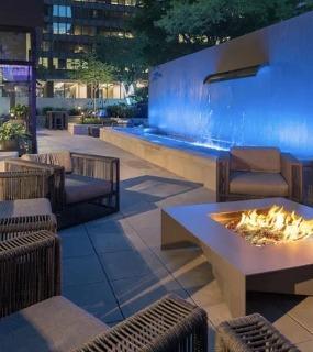 Outdoor lounge area with modern seating, a fire pit, and a beautifully lit waterfall feature at Columbus Plaza