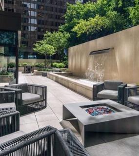 Outdoor lounge area with modern seating, a fire pit, and a cascading waterfall feature surrounded by greenery at Columbus Plaza