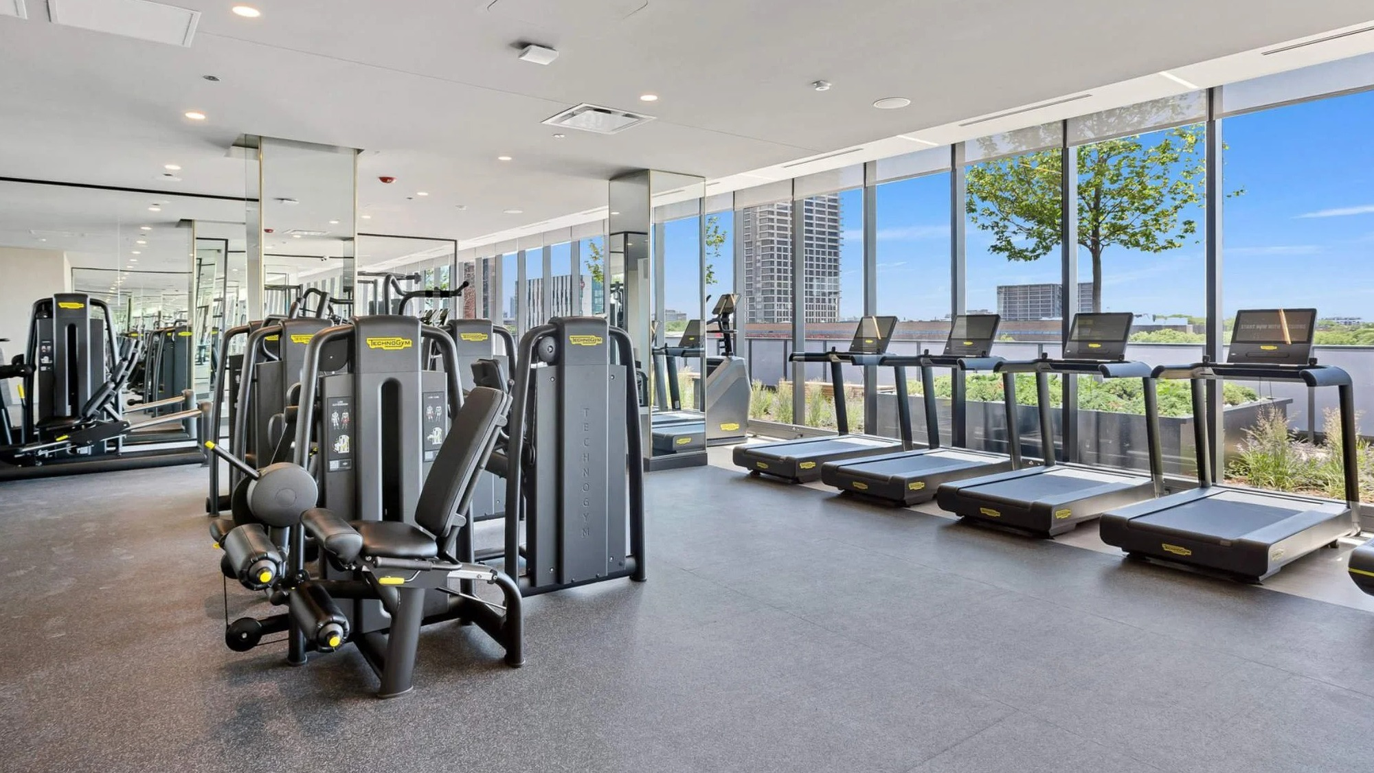 Well-equipped gym at Coppia apartments in Chicago with various cardio machines, weights, and large windows