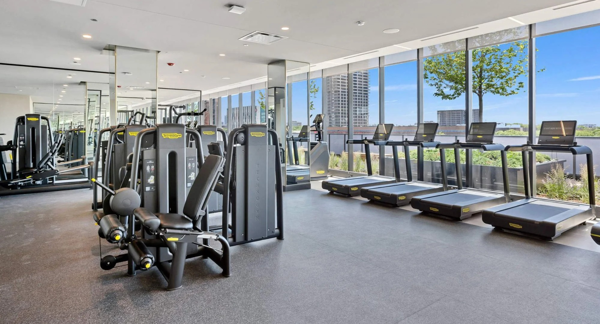 Well-equipped gym at Coppia apartments in Chicago with various cardio machines, weights, and large windows