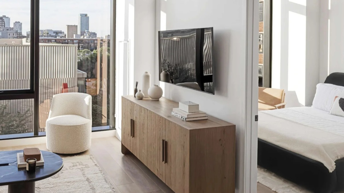 Bright living room at Coppia in Chicago with a mounted TV, modern credenza, and a peek into a cozy bedroom