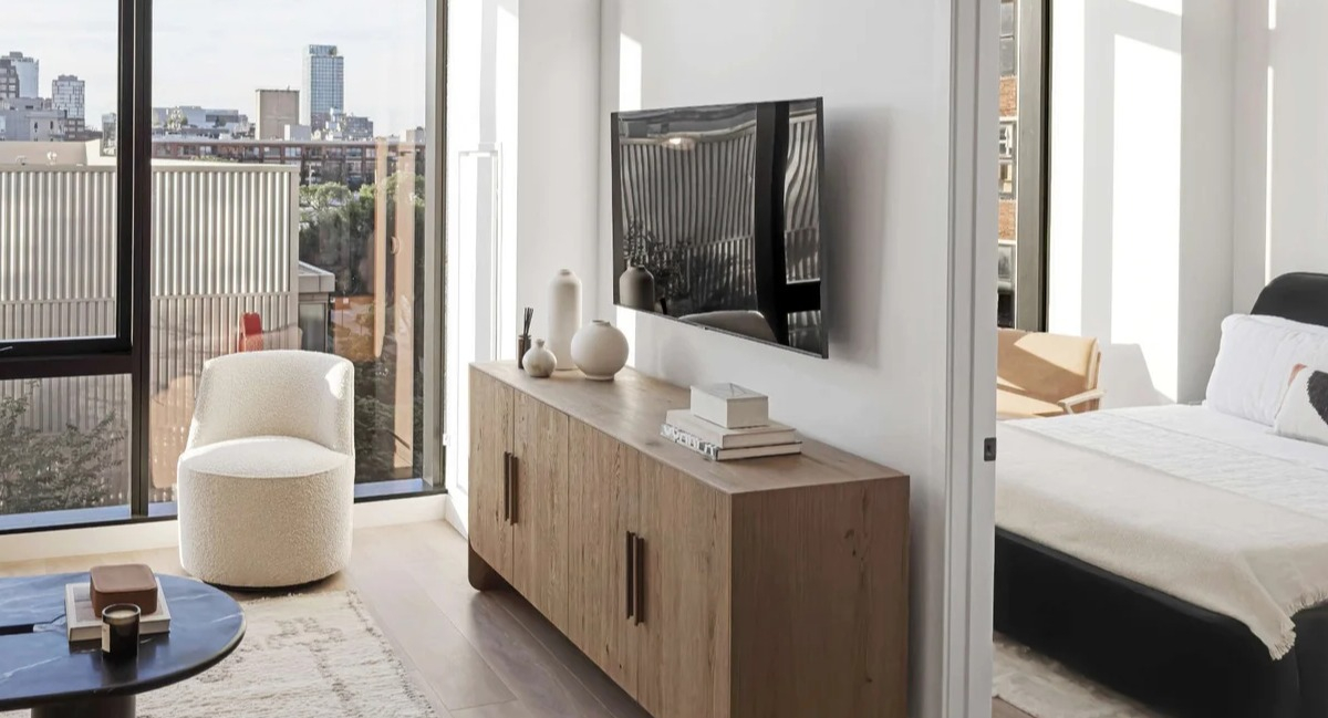 Bright living room at Coppia in Chicago with a mounted TV, modern credenza, and a peek into a cozy bedroom